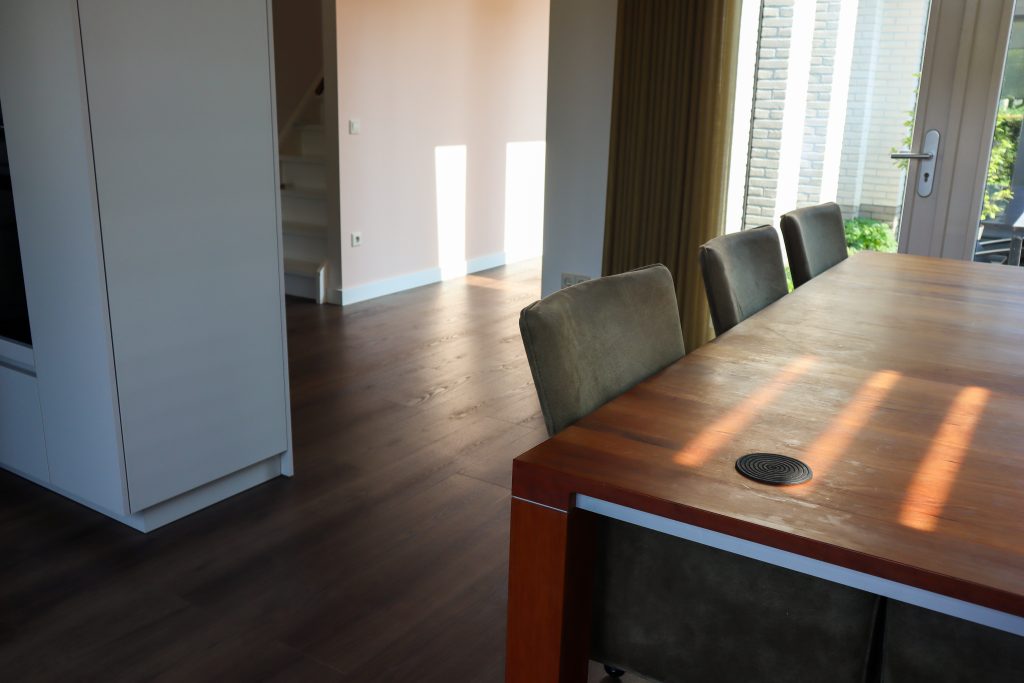 Eetkamer met houten tafel en stoelen bij trap.
