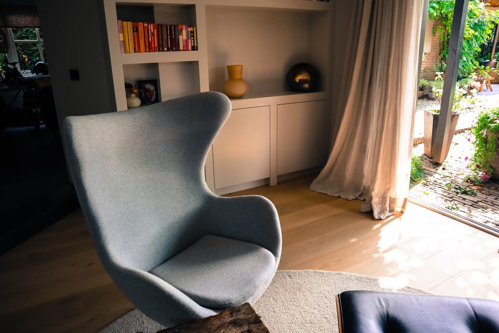 Moderne stoel in zonnige woonkamer met boekenkast.